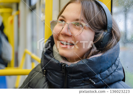 Smiling teenager girl with braces and headphones in tram during rainy weather Smiling teenager girl with braces and headphones in tram during rainy weather 136023223