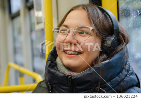 Smiling teenager girl with braces and headphones in tram during rainy weather Smiling teenager girl with braces and headphones in tram during rainy weather 136023224
