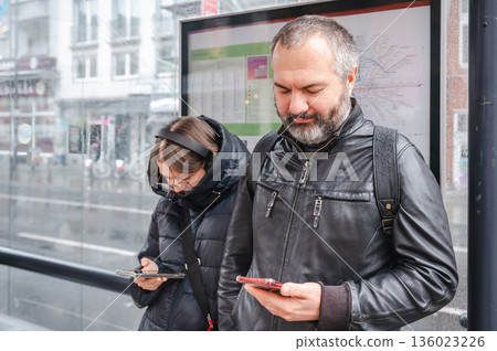 Father and daughter waiting for tram, looking at their smartphones Father and daughter waiting for tram, looking at their smartphones 136023226