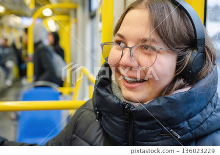 Smiling teenager girl with braces and headphones in tram during rainy weather Smiling teenager girl with braces and headphones in tram during rainy weather 136023229