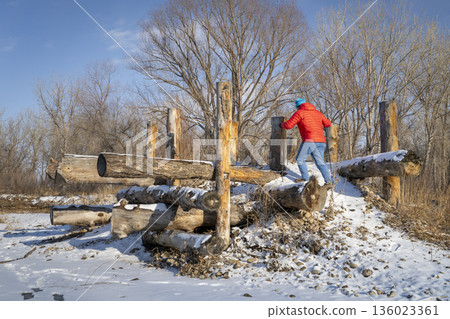 hiker with trekking poles is climbing a log erosion control structure on a shore of the Poudre RIver in Fort Collins, Colorado, cold winter scenery 136023361