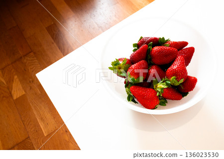 Fresh strawberries in a white bowl on wooden surface 136023530