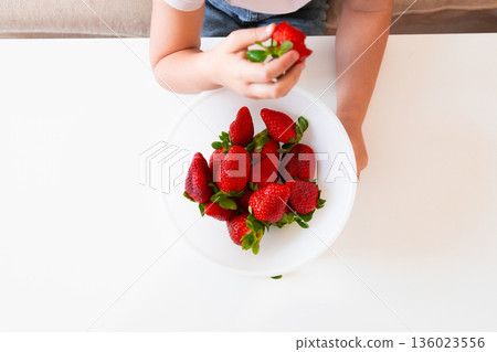 Child holding fresh strawberries on white plate Child holding fresh strawberries on white plate 136023556
