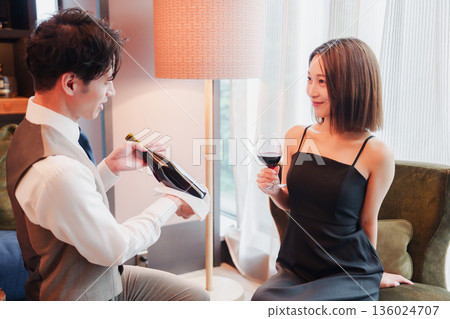 A male hotel room service staff member serving wine to a woman 136024707