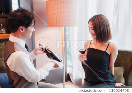一名男性酒店客房服務員正在為一位女士斟酒。 136024708