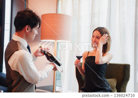 A male hotel room service staff member serving wine to a woman A male hotel room service staff member serving wine to a woman 136024710