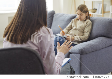 Therapist talking to child holding pencil to write in notebook during therapy Therapist talking to child holding pencil to write in notebook during therapy 136024773