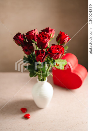 Valentine's Day festive background. Red roses flowers in a vase and heart gift box on neutral background. Festive greeting card, flat lay Valentine's Day festive background. Red roses flowers in a vase and heart gift box on neutral background. Festive greeting card, flat lay 136024859