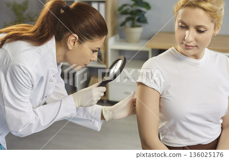 Young female doctor examining hand skin of woman patient in medical clinic. Young female doctor examining hand skin of woman patient in medical clinic. 136025176