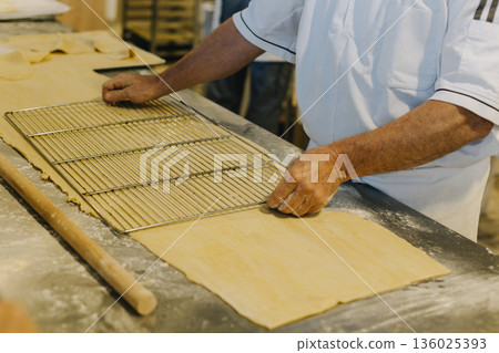Chef male hands working with dough on a table in a bakery. Chef male hands working with dough on a table in a bakery. 136025393