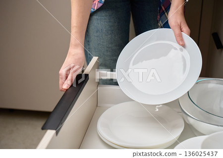 Hands placing white ceramic plates into kitchen drawer. Concept of home organization Hands placing white ceramic plates into kitchen drawer. Concept of home organization 136025437