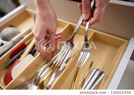 Hands holding metal forks above wooden organizer tray inside kitchen drawer. Concept of kitchen organization Hands holding metal forks above wooden organizer tray inside kitchen drawer. Concept of kitchen organization 136025438