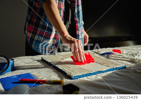 Hand pressing red plastic scraper into thick paste to shape circular textured lines Hand pressing red plastic scraper into thick paste to shape circular textured lines 136025439