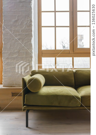 Modern khaki green velvet sofa near large window in stylish living room, loft interior 136025630