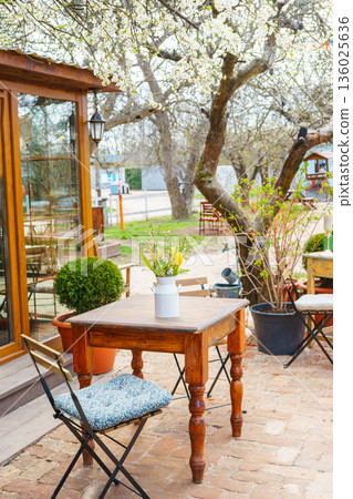 Spring outdoor garden table with bouquet of flowers under blooming trees in cozy backyard cafe Spring outdoor garden table with bouquet of flowers under blooming trees in cozy backyard cafe 136025636
