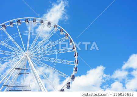 Large ferris wheel against blue sky with white clouds on sunny day 136025682