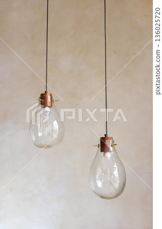 Handmade glass pendant lights hanging in minimalist interior space on painted wall background Handmade glass pendant lights hanging in minimalist interior space on painted wall background 136025720