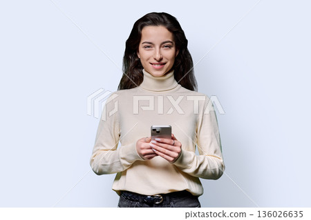 Portrait of smiling teenage girl holding smartphone on white studio background Portrait of smiling teenage girl holding smartphone on white studio background 136026635