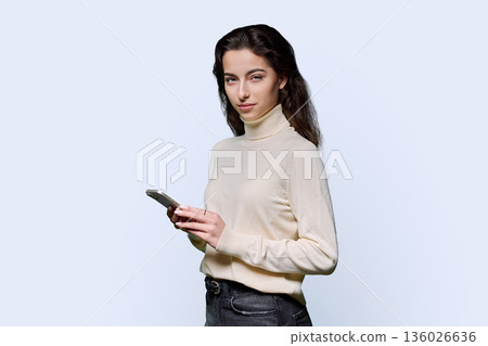 Portrait of serious teenage girl holding smartphone on white studio background Portrait of serious teenage girl holding smartphone on white studio background 136026636