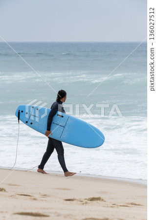 Surfer girl carrying a soft board Surfer girl carrying a soft board 136027512