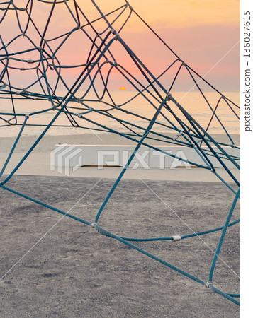 Playground rope structure against a captivating sunset over the ocean Playground rope structure against a captivating sunset over the ocean 136027615
