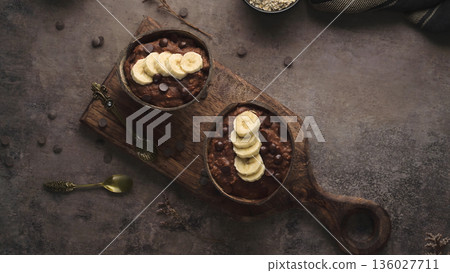 Chocolate Banana Protein Oatmeal in Coconut Bowls on a Rustic Wooden Board Chocolate Banana Protein Oatmeal in Coconut Bowls on a Rustic Wooden Board 136027711