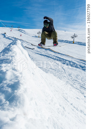 Snowboarder jumping against blue sky 136027799