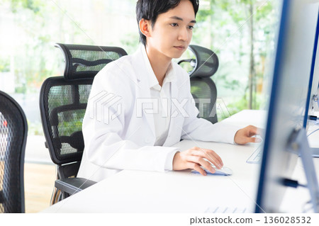 Male of white coat operating a personal computer Male of white coat operating a personal computer 136028532