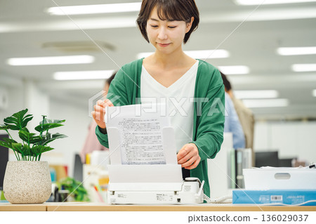 辦公室裡，一位女士正在傳送傳真。 136029037
