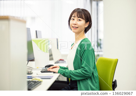 一位留著短髮的年輕女員工在辦公室做文書工作。 一位留著短髮的年輕女員工在辦公室做文書工作。 136029067