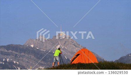 Hiker sets up tent near mountain summit at sunset with clear sky and vivid colors Hiker sets up tent near mountain summit at sunset with clear sky and vivid colors 136029530