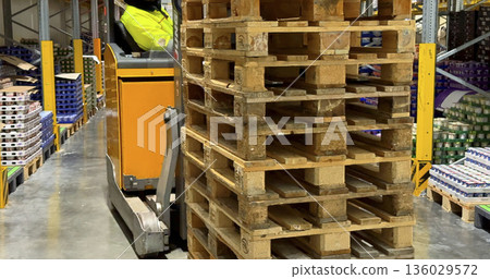 Worker moves wooden pallets in a warehouse during daytime in a busy storage area 136029572