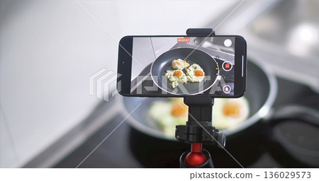 Cooking eggs in a pan while recording the process with a smartphone setup in a kitchen space 136029573