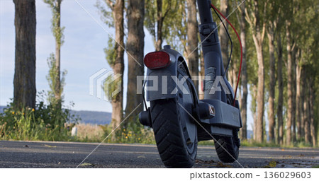 Electric scooter parked on a quiet path lined with trees near open fields during daylight hours Electric scooter parked on a quiet path lined with trees near open fields during daylight hours 136029603