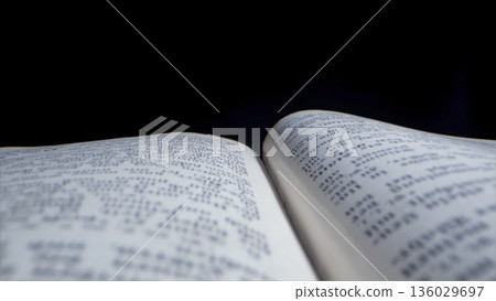 Open book with pages displaying text, placed on a dark surface, close view captures printed words and layout clearly 136029697