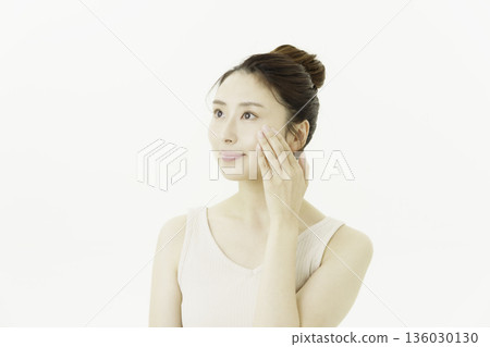 A young Japanese woman wearing a tank top and updo on a white background checking the wrinkles around her eyes 136030130