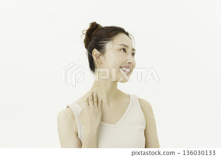 A young Japanese woman wearing a tank top against a white background and touching her neck 136030133