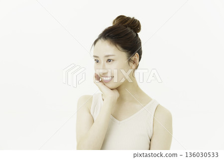 一位年輕的日本女性穿著背心，頭髮盤起，面帶微笑，手撫臉頰，背景是白色。 136030533