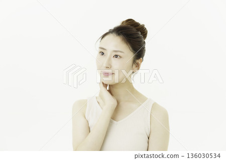 A young Japanese woman wearing a tank top against a white background and touching her neck 136030534