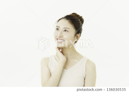 A young Japanese woman wearing a tank top against a white background and touching her neck 136030535