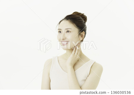 一位年輕的日本女子穿著背心，在白色背景前，撫摸著自己的脖子。 136030536