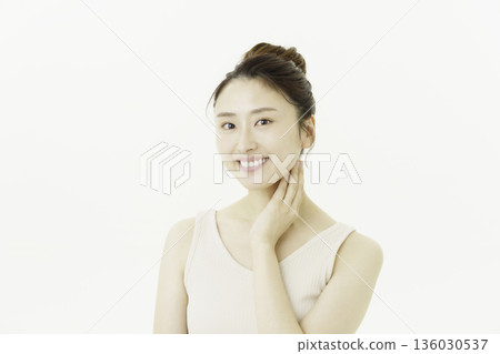 A young Japanese woman wearing a tank top against a white background and touching her neck 136030537