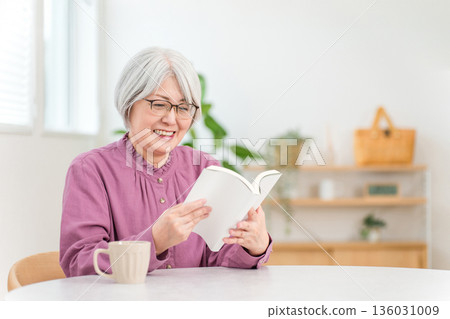 一位銀髮蒼蒼的亞裔老婦人坐在桌旁讀書。 136031009