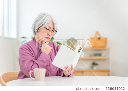 一位銀髮蒼蒼的亞裔老婦人坐在桌旁讀書。 136031012