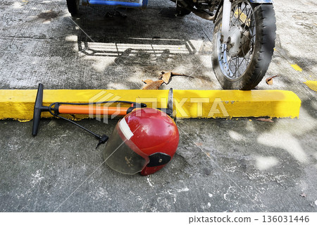 motorcycle helmet and air pump on concrete ground next to yellow parking barrier and vehicle wheel in bright sunlight 136031446