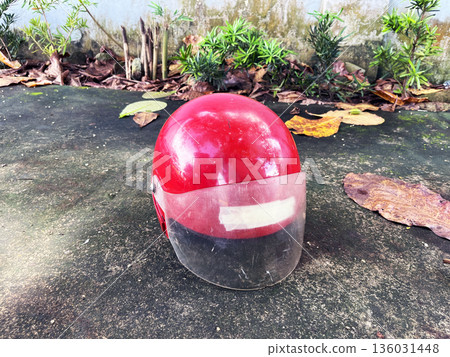 worn red motorcycle helmet with a scratched visor resting on a concrete ground outdoors worn red motorcycle helmet with a scratched visor resting on a concrete ground outdoors 136031448