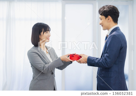 A woman giving a gift to a man in the office A woman giving a gift to a man in the office 136032381