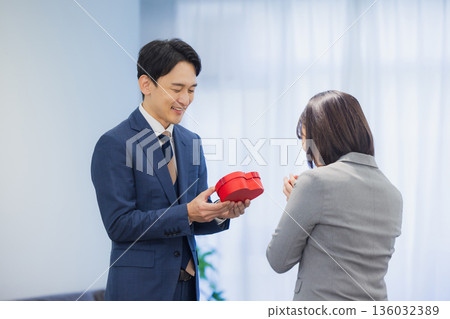 辦公室裡,一位女士送給一位男士一份禮物。 辦公室裡,一位女士送給一位男士一份禮物。 136032389