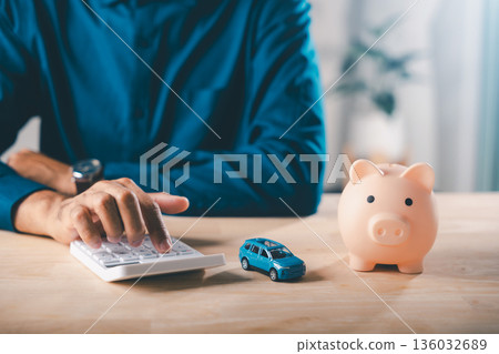 Man calculates auto car loan payments, managing piggy bank money, saving for insurance, bank debt, tax, planning financial safety, securing future investment Man calculates auto car loan payments, managing piggy bank money, saving for insurance, bank debt, tax, planning financial safety, securing future investment 136032689
