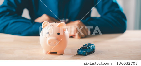 Pink piggy bank sits by blue toy car, man organizes car money bank insurance piggy save auto loan cost finance fuel saving tax during personal vehicle purchase budget planning Pink piggy bank sits by blue toy car, man organizes car money bank insurance piggy save auto loan cost finance fuel saving tax during personal vehicle purchase budget planning 136032705